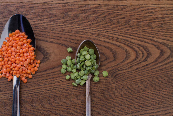 Cerca de lentejas naranjas y guisantes verdes divididos en cucharas de metal
. - Foto, Imagen