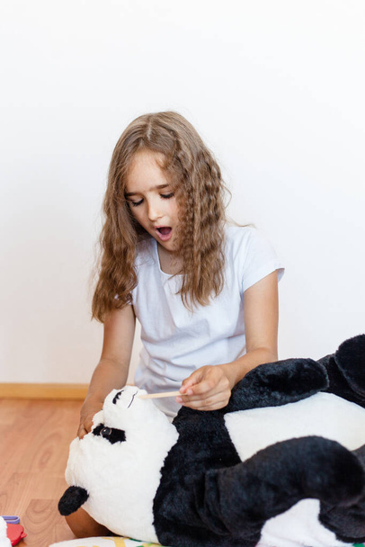 Girl, school girl treats her toy bear, Panda, bear got sick, playing doctor, veterinarian, role, growing up, learning in the game - 写真・画像