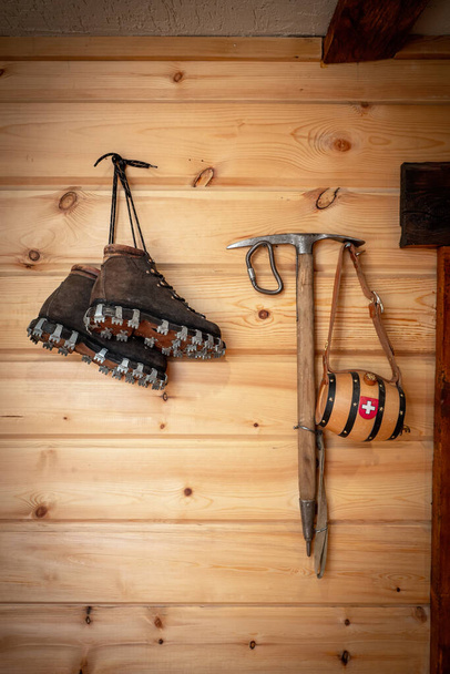 Vintage climbing leather boots and ice ax hang on a wooden wall. Antique Climbing Equipment - Photo, Image