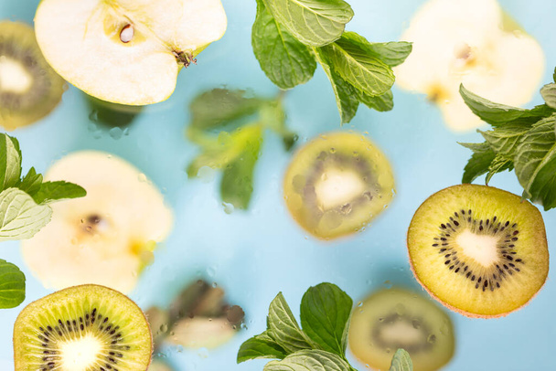 Apples, kiwi and mint leaves in flight. Fresh spring texture leaves of different sizes on blue background - Foto, Imagen