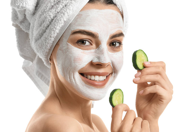 Mooie jonge vrouw met komkommer plakken en gezichtsmasker op witte achtergrond - Foto, afbeelding