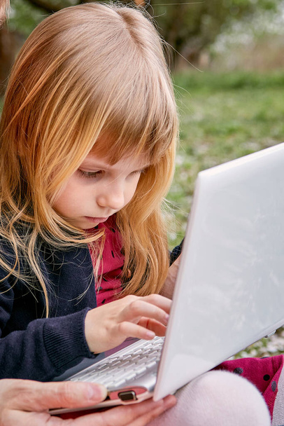 Little girl with a laptop and study in a flowered garden. Against the background of sun rays and flowering trees. - Fotoğraf, Görsel