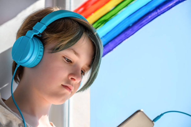 Sad teenage girl in headphones listening to music, leaning on the window. Misses her friends. - Foto, Bild