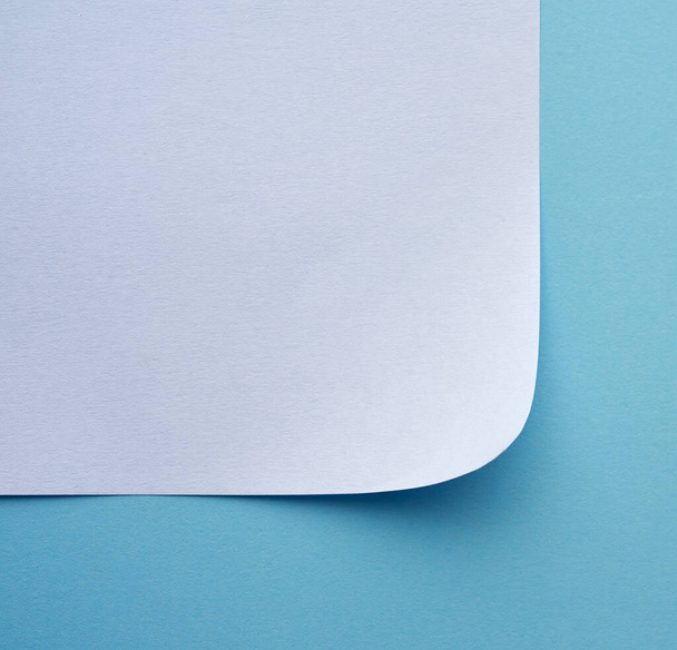 загорнутий лист білого паперу на синьому фоні, макрос, вид зверху
 - Фото, зображення