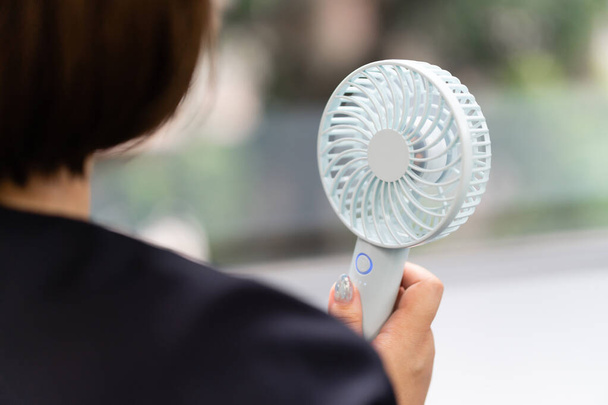 Uma mulher japonesa se aquece ao vento de um ventilador portátil
 - Foto, Imagem