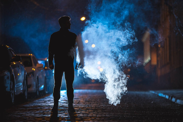 Mężczyzna stoi w pobliżu dymu. Wieczorna noc. Ujęcie teleobiektywu - Zdjęcie, obraz
