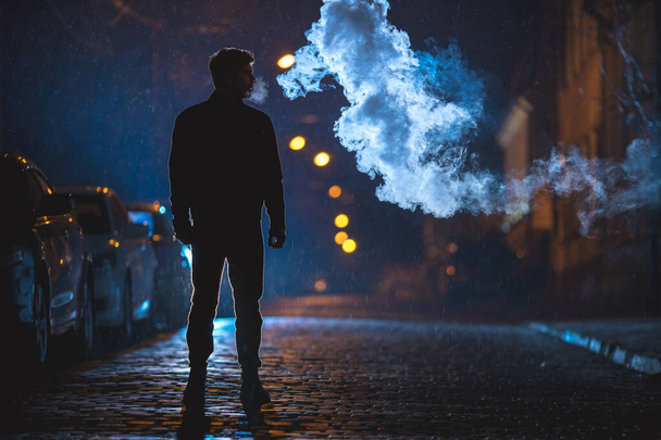 The man stand near the cloud of smoke. Evening night time - Zdjęcie, obraz