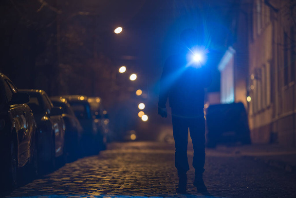 Ο άνθρωπος με το φακό στέκεται σε βρεγμένο δρόμο. Βραδινή νύχτα - Φωτογραφία, εικόνα