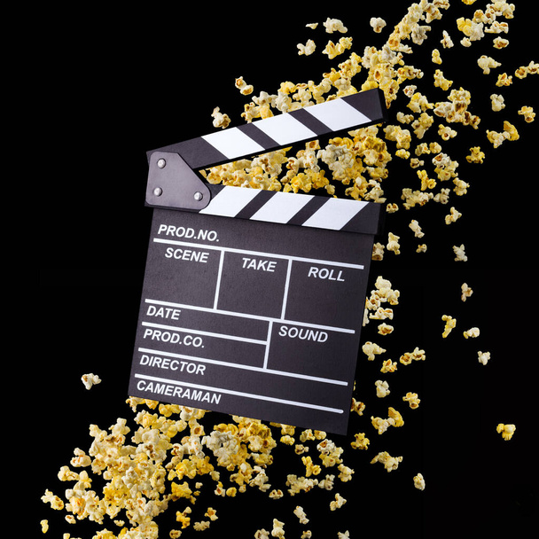 Flying popcorn en film clapper board geïsoleerd op zwarte achtergrond - Foto, afbeelding