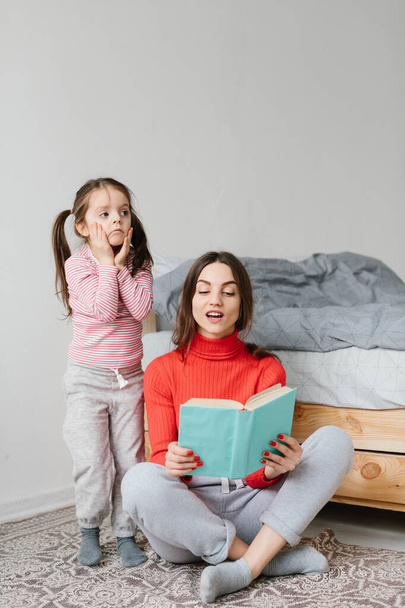 Bonne mère de famille et fille enfant lecture tenant livre couché dans le lit, maman souriante baby sitter racontant conte de fées drôle à mignon enfant d'âge préscolaire fille s'amuser à rire avec des histoires au coucher
 - Photo, image