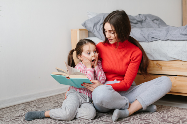 Happy family mother and child daughter reading holding book lying in bed, smiling mom baby sitter telling funny fairy tale to cute preschool kid girl having fun laughing together with bedtime stories - Foto, imagen
