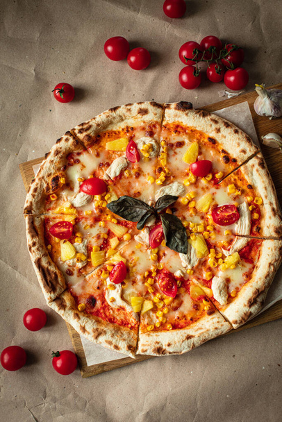 Pizza na widoku zarządu. Soczysta pizza z kurczakiem, ananasem i czerwonymi pomidorami na drewnianej planszy i papierze Kraft - Zdjęcie, obraz