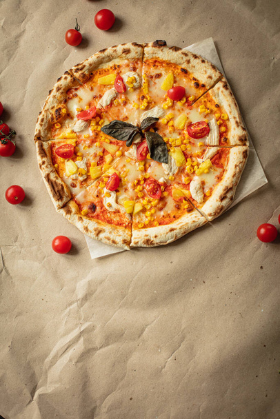 Ronde pizza voor een spandoek op Kraftpapier en houten plank. Pizza met kaas, kip, ananas, thuis gekookte tomaten. - Foto, afbeelding