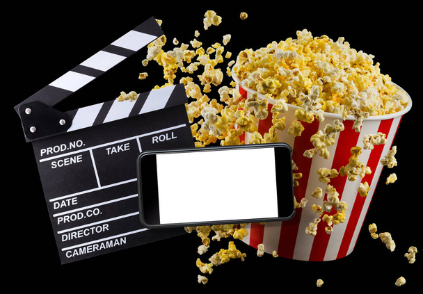 Flying popcorn, film clapper board and phone isolated on black background - Foto, Bild