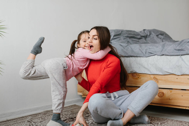 Happy family mother and child daughter reading holding book lying in bed, smiling mom baby sitter telling funny fairy tale to cute preschool kid girl having fun laughing together with bedtime stories - Foto, Imagen