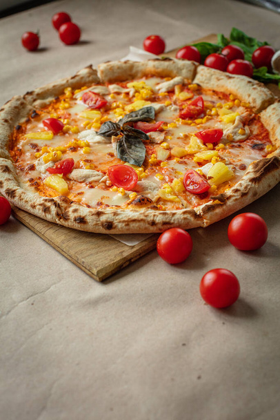 Pizza hecha en madera y papel Kraft, alrededor de tomates, hierbas y ajo. Almuerzo preparado en casa
 - Foto, Imagen