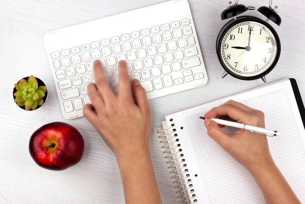 Online education. Home schooling at quarantine and self isolation during coronavirus. Flat lay with white keyboard, apple, alarm clock and hands - Photo, Image
