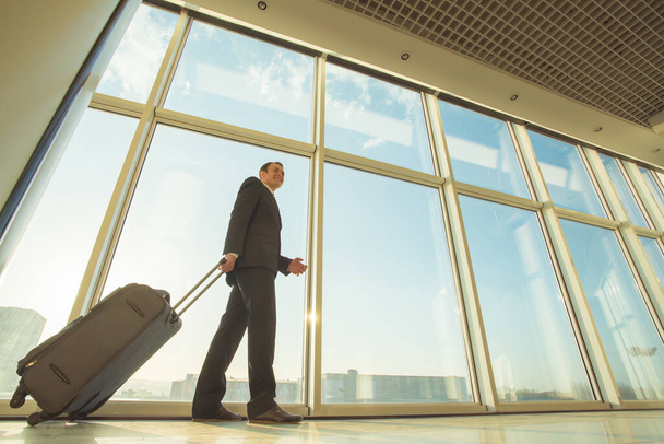 Ο επιχειρηματίας περπατάει με μια βαλίτσα κοντά σε πανοραμικά παράθυρα - Φωτογραφία, εικόνα