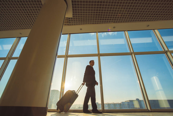 El empresario camina con una maleta cerca de ventanas panorámicas
 - Foto, Imagen