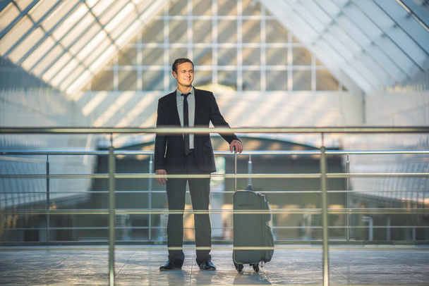 Счастливый человек стоит с чемоданом в бизнес-центре
 - Фото, изображение