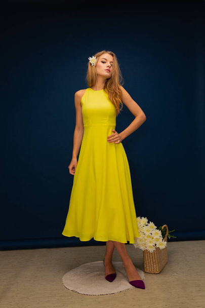 mladá krásná blondýna dívka ve žlutých letních šatech a žluté boty s květinami na modrém pozadí studia - Fotografie, Obrázek