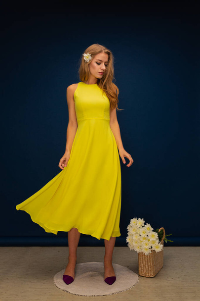 молода красива блондинка в жовтій літній сукні і жовті туфлі з квітами на синьому студійному фоні
 - Фото, зображення
