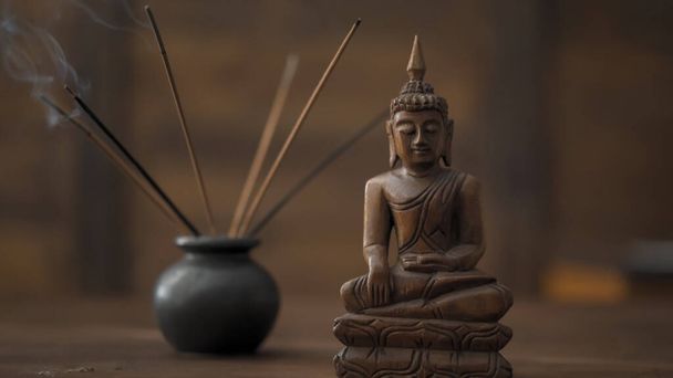 Wooden statuette of Buddha incense sticks at workplace. Abstract picture of a modern office in oriental style, selective focus on smoking incense sticks and wooden buddha figurine at table - Foto, Imagen
