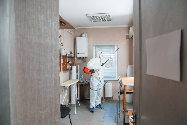 Coronavirus Pandemic. A disinfector in a protective suit and mask sprays disinfectants in the house or office - Foto, afbeelding