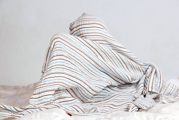 Small Caucasian boy playing under a striped blanket on white duvet bedding - Photo, image