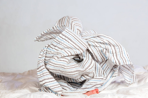 Small Caucasian boy playing under a striped blanket on white duvet bedding - Zdjęcie, obraz