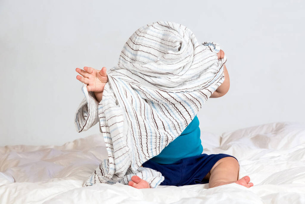 Small Caucasian boy playing under a striped blanket on white duvet bedding - Foto, imagen