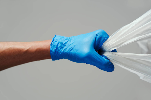 Крупный план человека в синих латексных перчатках с белым пакетом покупок в руке
 - Фото, изображение