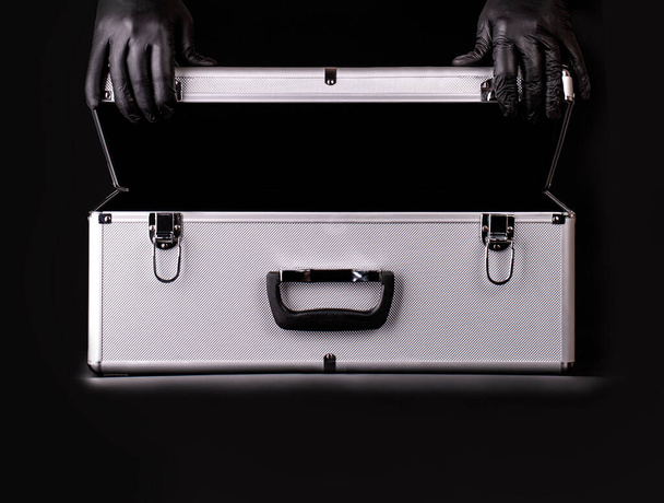 Η μεγάλη βαλίτσα αλουμινίου και τα χέρια μαύρα γάντια ασφαλείας - Φωτογραφία, εικόνα