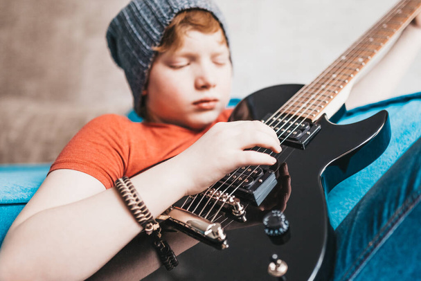 Closeup of a child playing a black electric guitar - hand picks up the notes on the strings - selective focus - Fotó, kép