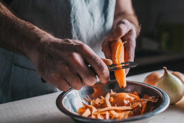 A qualified chef cleans ripe orange carrots in the kitchen with a special knife - home cooking - Fotografie, Obrázek