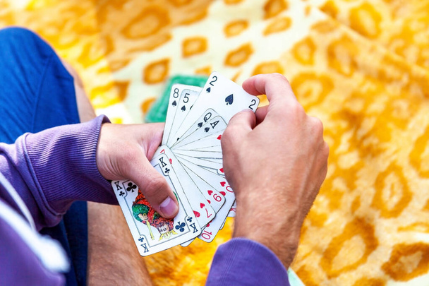 Nuori mies rento vaatteet pelaa korttia istuu blaket ulkopuolella, kädet lähikuva, poiminta yksi kortti kaksi pataa, tilalla koko pakan levittää Korttipeli ulkoilu yksinkertainen abstrakti käsite
 - Valokuva, kuva
