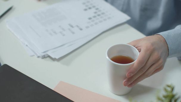 Kantoormedewerker legt documenten neer en drinkt thee - Foto, afbeelding