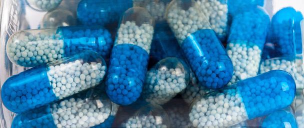 Veel blauw wit twee kleuren transparante supplement pillen met granulaat, medicatie in een te zien door de fles, vervagen. Veel grote vitaminecapsules zichtbaar via een plastic verpakking. Geneeskundige achtergrond - Foto, afbeelding