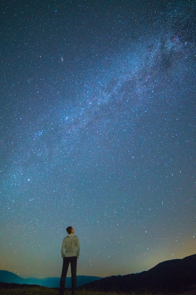 Adam duruyor ve yıldızlı gökyüzüne bakıyor. Gece vakti. - Fotoğraf, Görsel