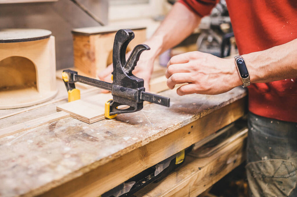 Carpentry workshop - a man fixes wooden parts with glued clamps - Fotó, kép