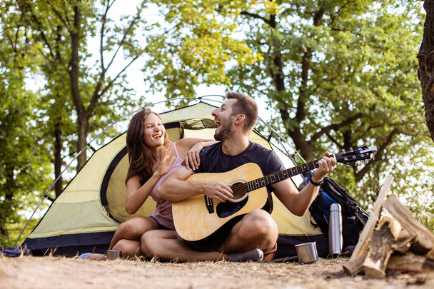 A man plays for a woman on a guitar near a tent at sunset. Honeymoon in the hike - Foto, Imagen