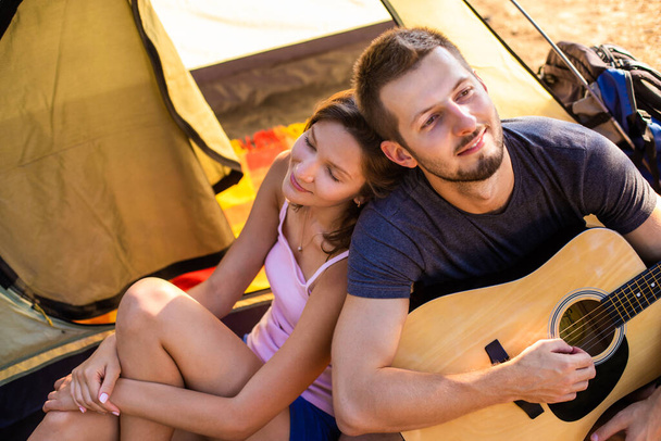 Un homme joue pour une femme à la guitare près d'une tente au coucher du soleil. Lune de miel dans la randonnée
 - Photo, image