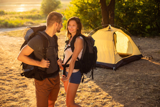 A man and a woman in a hiking trip with backpacks near a tent at sunset. Honeymoon in nature - Foto, Bild