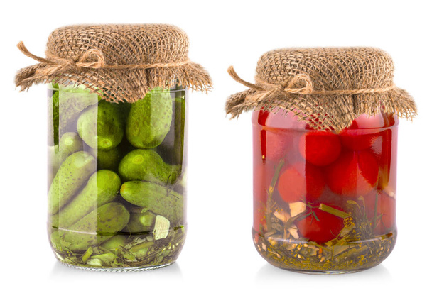 Los frascos de vidrio con tomates y pepinos con tapa de arpillera sobre fondo blanco
 - Foto, imagen