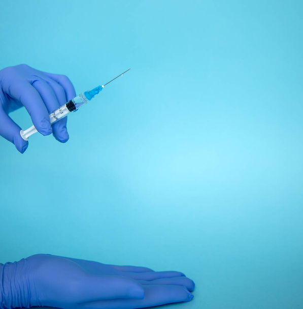 Der Arzt hält eine Spritze. Injektion mit Medikamenten. Mediziner in blauen Handschuhen. Impfung in einer Spritze. Kosmetische Verfahren. Die Krankenschwester wird eine Spritze geben - Foto, Bild
