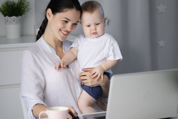 Young mother working in a decree at the computer with a baby son in her arms - Fotografie, Obrázek