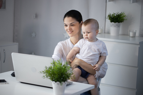 Jeune mère travaillant dans un décret à l'ordinateur avec un bébé fils dans ses bras
 - Photo, image