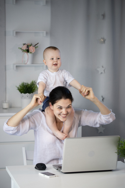 Молода мати працює в указі за комп'ютером з сином на руках
 - Фото, зображення