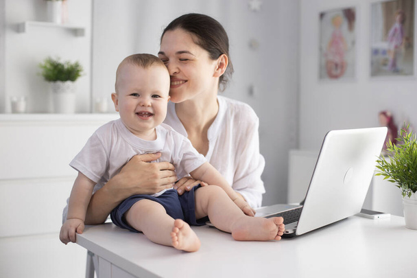 Young mother working in a decree at the computer with a baby son in her arms - Foto, afbeelding