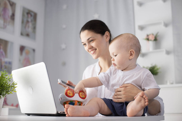 Jonge moeder werkt in een decreet aan de computer met een zoontje in haar armen - Foto, afbeelding